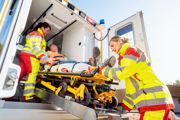 Ensihoitajat laittavat loukkaantuneen miehen paareille ambulanssiautoon - Valokuva, kuva