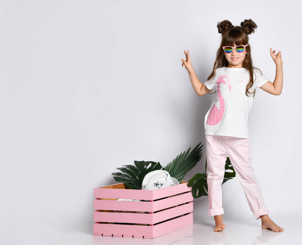 Een mooi meisje poseert naast een roze houten doos, draagt een Flamingo t-shirt en een zonnebril - Foto, afbeelding