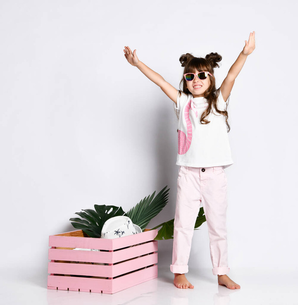 A beautiful girl poses next to a pink wooden box, wearing A Flamingo t-shirt and sunglasses, barefoot - Fotografie, Obrázek