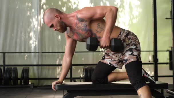 Mladý svalnatý vytetovaný silný sval vousatý evropský muž dělá tvrdé cvičení s činkami na ramena paže zpět na kříž fit trénink     - Záběry, video