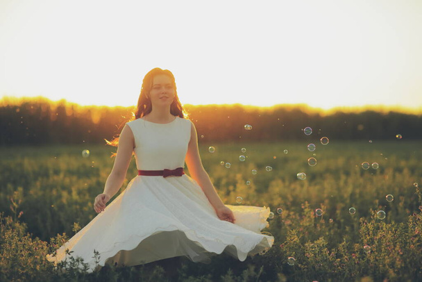 Piękna dziewczyna tańcząca w parku w świetle zachodu słońca. Bańki mydlane. Koncepcja szczęścia. Wysokiej jakości zdjęcie - Zdjęcie, obraz