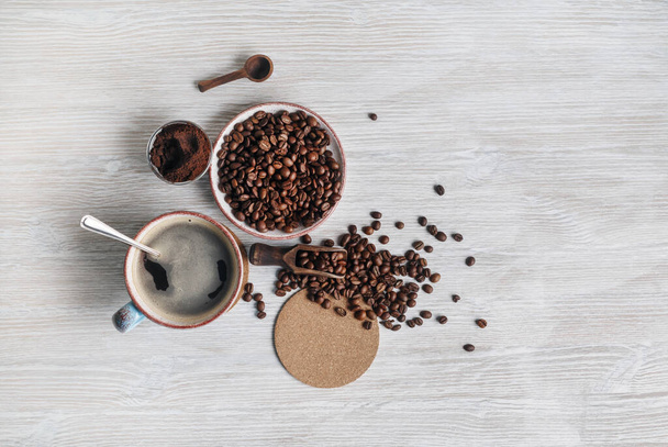 Photo of fresh tasty coffee on light wooden background. Coffee cup, coffee beans, ground powder and beer coaster. Top view. Flat lay. - Valokuva, kuva