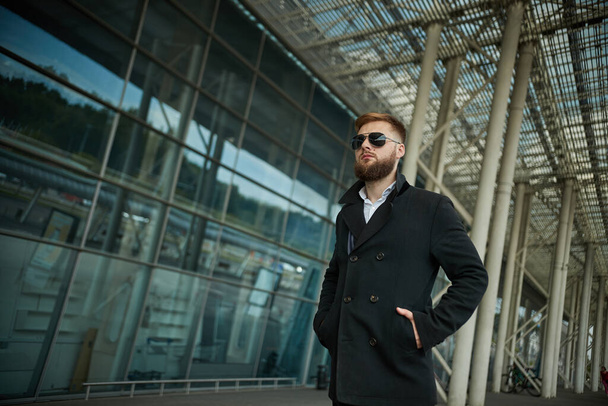 Success. Stylish young bearded man in coat, sunglasses businessman standing - Foto, Imagen