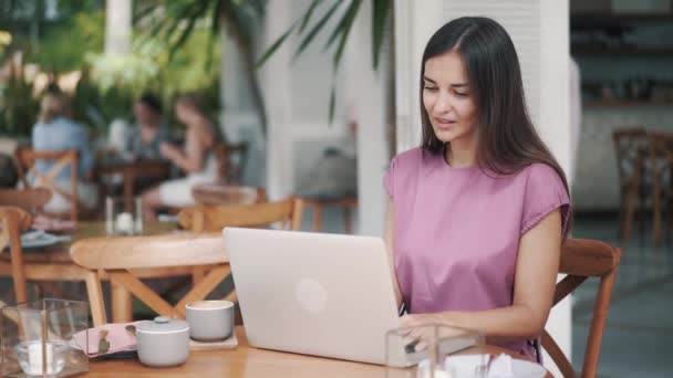 Beautiful woman sitting at table and using laptop for work in cafe - Video