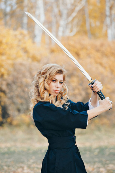 European woman with a katana in a kimono. the girl trains martial arts. a woman in the autumn forest. a warrior with a cold weapon in his hands - Foto, Imagen