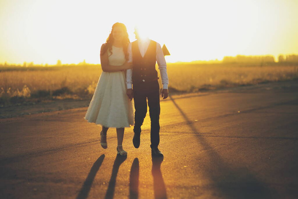 Morsian ja sulhanen pitävät toisiaan kädestä, halaavat ja kävelevät puistossa. Auringonlaskun valo. häät. Onnellisen rakkauden käsite. Laadukas kuva - Valokuva, kuva