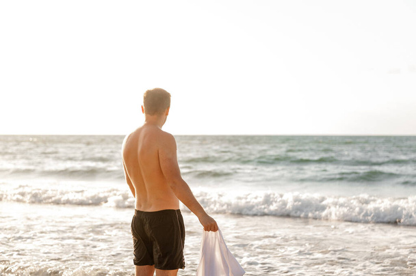 Mies valmistautuu kylpyyn meressä, pitäen t-paitaa, jonka hän otti pois - Valokuva, kuva