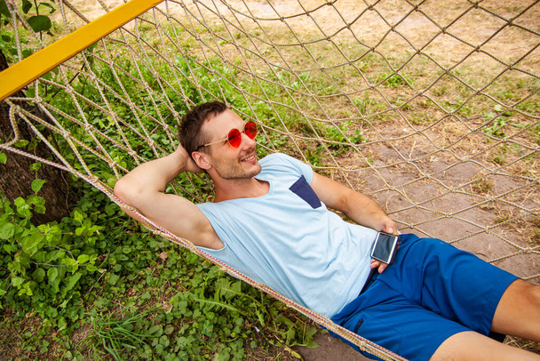 Young Happy Handsome Man Smiling In Hammock With Smartphone. - Photo, Image