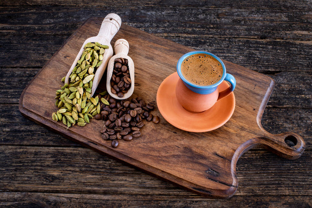 Kawa w tradycyjnym kubku i ziarna kawy na drewnianym stole. Kawa podawana na desce do krojenia.  - Zdjęcie, obraz