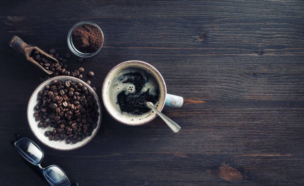 Вкусный свежий кофе. Кофейная чашка, кофейные зёрна, молотый порошок и стаканы на фоне старинного деревянного стола. Плоский лежал
. - Фото, изображение