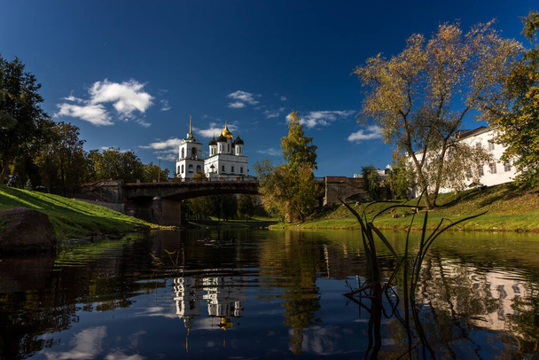 View of the Pskov Kremlin over the bridge at the city river on a summer clear day. The blue bright sky with clouds is reflected in a smooth surface of water. - Photo, Image
