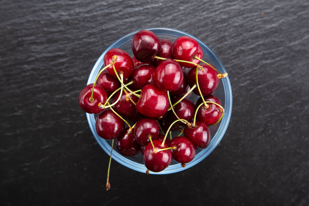 Ripe sweet cherry in black plate on dark stone background. Summer fresh berries for healthy diet. Top view, copy space. - Photo, image