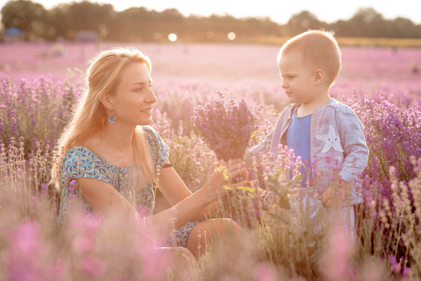Happy young mother and her little son posing in purple field of lavender flowers - Photo, Image