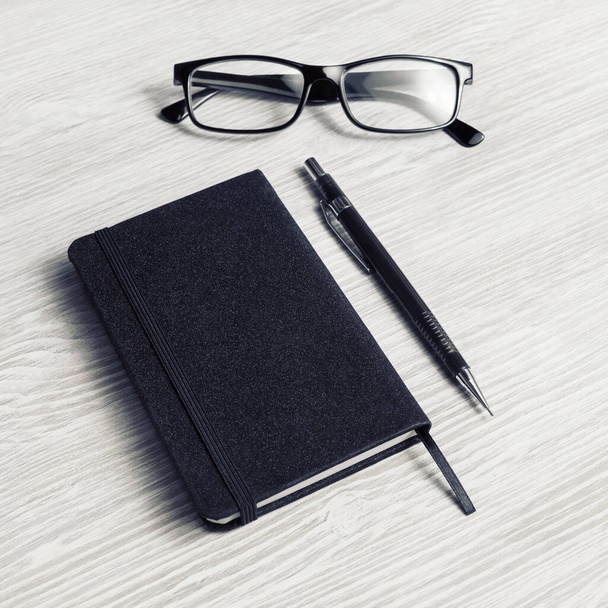 Blank black notepad, glasses and pencil on light wooden background. - Fotoğraf, Görsel