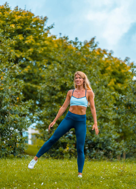 Fitness session with a young blonde Caucasian woman exercising on the street with a blue maya on her feet and a white short shirt. Performing side jumps - Фото, зображення