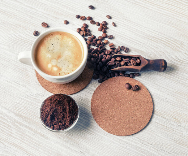 Delicious fresh coffee. Coffee cup, coffee beans, beer coaster and ground powder on light wooden background. Flat lay. - Photo, Image