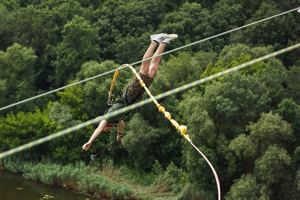Het concept van extreme sport en plezier. Een man is een sensatiezoeker en een touw springer van de brug. Hij is erg blij om een droom waar te maken. Hij houdt een actiecamera vast en is waanzinnig blij. - Foto, afbeelding