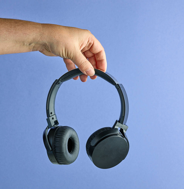 Black wireless headphones in human hand on blue background - Photo, Image