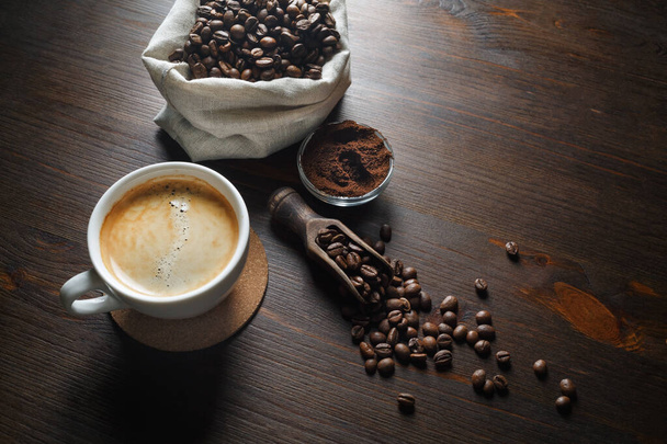 Coffee cup, coffee beans and ground powder on wooden kitchen table background. - Photo, Image