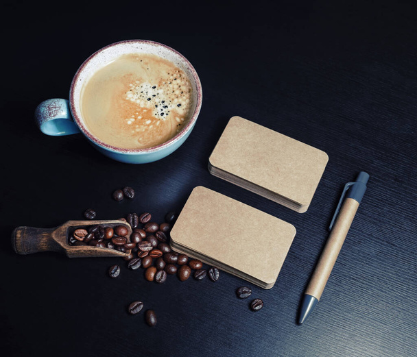 Blank kraft business cards, coffee cup, pen and coffee beans on black wooden background. Template for graphic designers portfolios. - Φωτογραφία, εικόνα