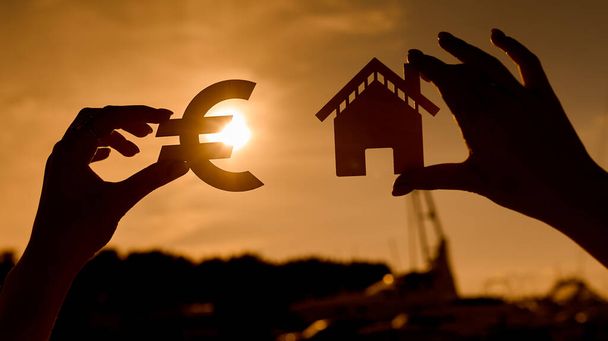 Euro σύμβολο και το σπίτι σε γυναικεία χέρια controunded στο ηλιοβασίλεμα - Φωτογραφία, εικόνα