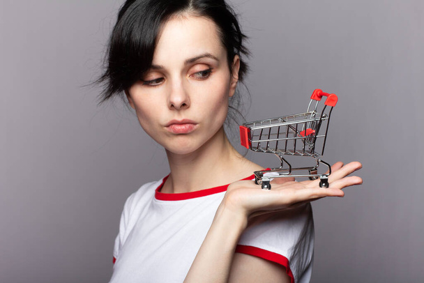 woman holds a small trolley from the store, gray background - Photo, Image
