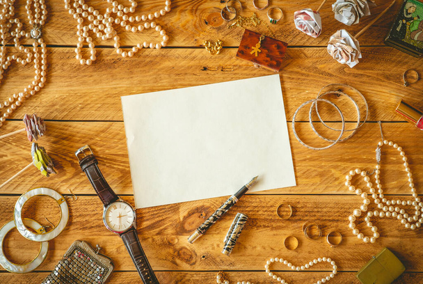 Uma folha de papel em branco para escrever uma carta em uma mesa de madeira com algumas memórias e jóias
 - Foto, Imagem