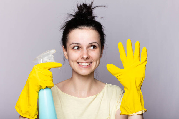Beautiful happy housewife with rubber gloves with finger near chin - Foto, Imagem