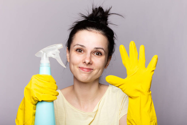 Beautiful happy housewife with rubber gloves with finger near chin - Фото, изображение