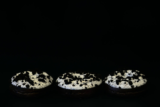 Три пончика с белой глазурью и коричневой горошек лежат бок о бок на темном фоне с большим количеством места для текста
 - Фото, изображение