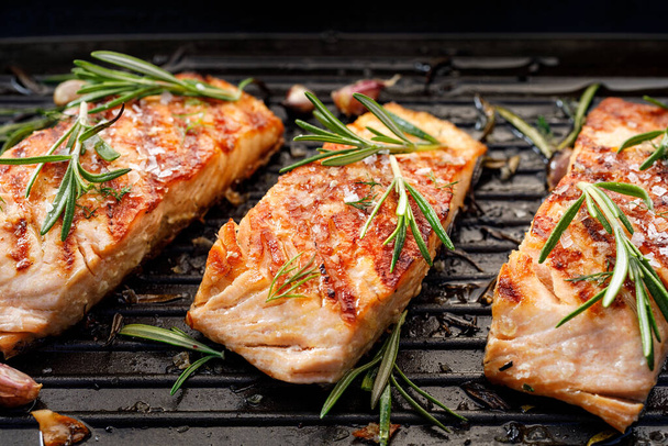 Grilled salmon fillets sprinkled with fresh herbs on a grill plate close up view - Photo, Image