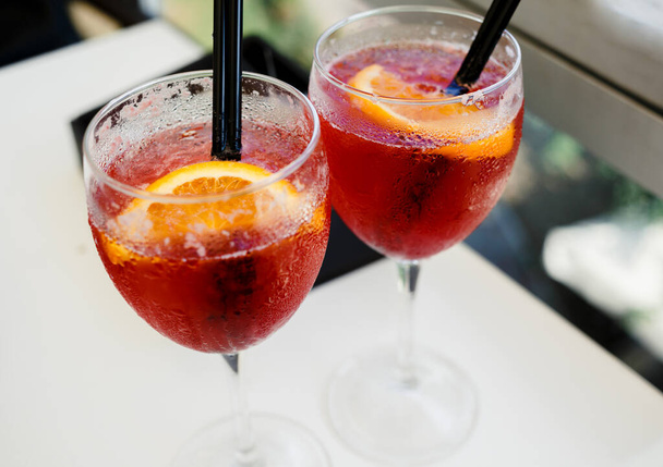 Closeup glasses of cocktail decorated with oranges on the table. Colorful pink soft drinks with ice and straws in a cafe - Φωτογραφία, εικόνα