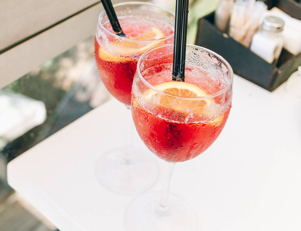 Крупные бокалы коктейля украшены апельсинами на столе. Красочные розовые безалкогольные напитки со льдом и соломинками в кафе - Фото, изображение
