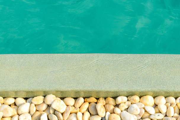 Fechar-se da borda de pedra em frente à piscina azul brilhante. Decoração e design de piscinas com reflexão da luz solar, férias, relaxar, escapadela
 - Foto, Imagem