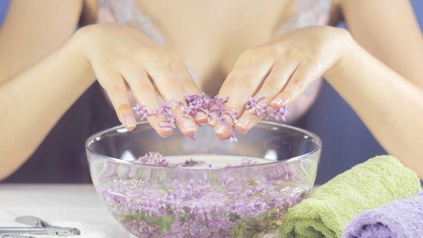 Hands of a woman in a bath with flowers. Manicure, nail SPA. Sensuality, skincare, feminine, salon, wash, wealth, therapy, cosmetics, treatment, relax, dayspa, aromatherapy - Фото, зображення