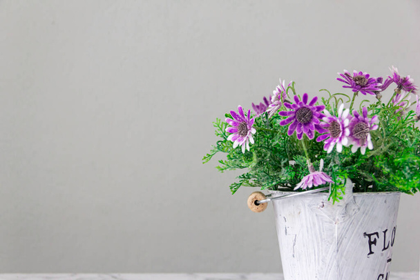 Επιλέξτε εστίαση στην γλάστρα. Πολύχρωμα ψεύτικα λουλούδια με πράσινα φύλλα στο καλάθι Ένας κουβάς σε καφέ ξύλινο τραπέζι σε καφετέρια το πρωί Πλαστική γλάστρα Εσωτερικοί χώροι, γραφεία και διακόσμηση σαλονιού - Φωτογραφία, εικόνα