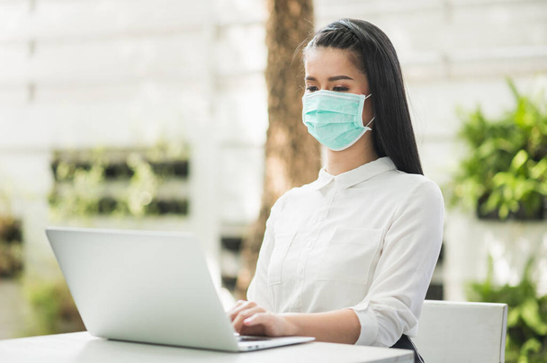 Beautiful asian woman wearing protection mask work from home in the morning. Young asian female with laptop stay at home. - Photo, Image