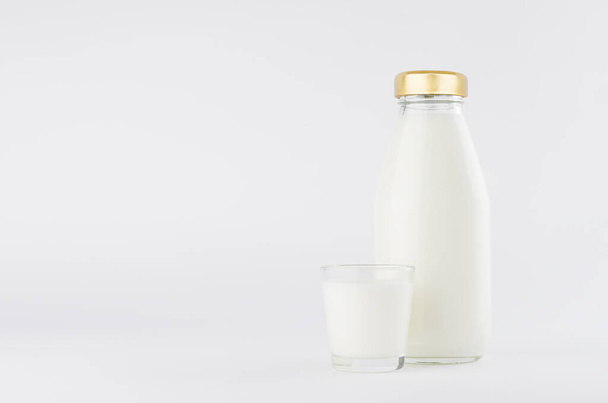 Milch in Glasflasche mit goldener Kappenschablone mit Glas auf weißem Hintergrund mit Kopierraum, Attrappe. - Foto, Bild