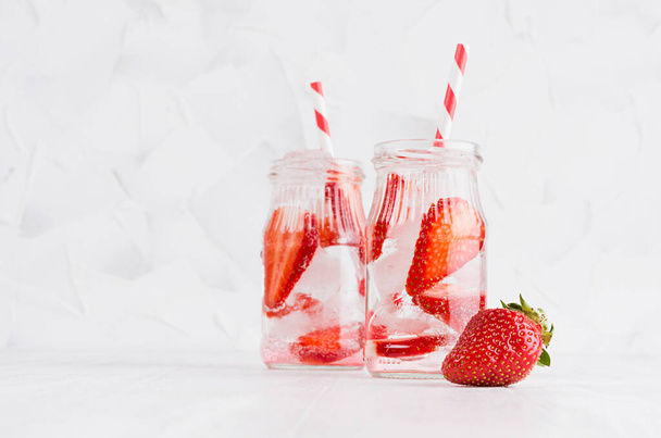 Summer homemade drinks - infused strawberry water with sliced berry, ice cubes, soda, straw in soft light white interior, copy space. - Fotografie, Obrázek