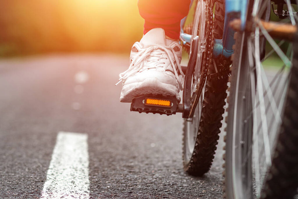 Benen op de pedalen van een fiets close-up, rijden op een weg in het bos. Het concept van een gezonde levensstijl, cardiotraining. Kopieerruimte - Foto, afbeelding