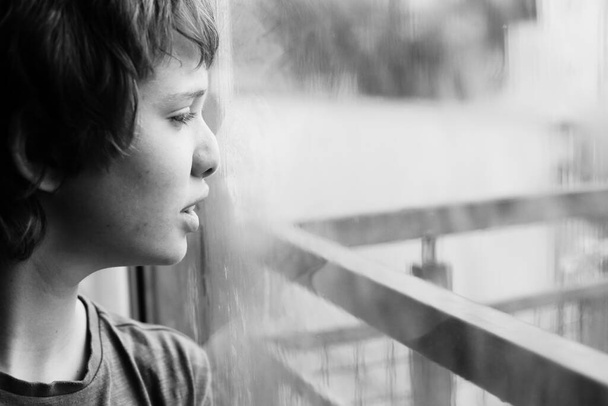 Χαριτωμένο 12χρονο αυτιστικό αγόρι κοιτάζει μέσα από το παράθυρο - Φωτογραφία, εικόνα