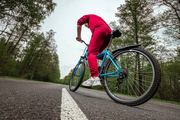 A man in a tracksuit on a bicycle rides on a road in the forest. The concept of a healthy lifestyle, cardio training. Copyspace - Fotografie, Obrázek