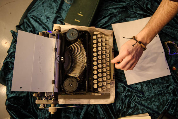 πάνω όψη της δακτυλογράφησης χεριών του ανθρώπου σε vintage γραφομηχανή σε ένα κομμάτι εφημερίδας και σκούρο μπλε βελούδινο ύφασμα στο πάτωμα  - Φωτογραφία, εικόνα