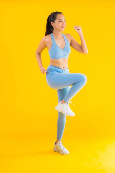Porträt schöne junge asiatische Sportlerin mit Sportbekleidung bereit für die Übung auf gelbem isolierten Hintergrund - Foto, Bild