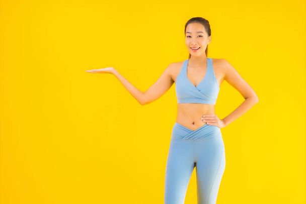 Portret mooie jonge aziatische sport vrouw met sportschoeisel klaar voor oefening op geel geïsoleerde achtergrond - Foto, afbeelding