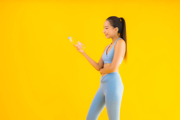 Portret piękna młoda azjatycka kobieta z butelką wody na żółtym odizolowanym tle - Zdjęcie, obraz