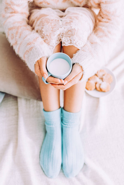 Young woman on the bed with with cup of milk in hands enjoys her stay at home. - Foto, imagen