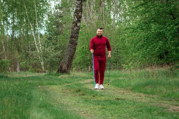 A man in a tracksuit is engaged in Nordic walking. The concept of a healthy lifestyle, cardio training. Copyspace - Fotoğraf, Görsel