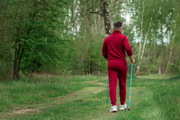 A man in a tracksuit is engaged in Nordic walking. The concept of a healthy lifestyle, cardio training. Copyspace - Foto, imagen