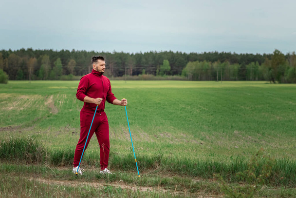 Ein Mann im Trainingsanzug ist mit Nordic Walking beschäftigt. Das Konzept eines gesunden Lebensstils, Ausdauertraining. Kopierraum - Foto, Bild